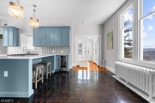 kitchen featuring radiator, light countertops, blue cabinets, beverage cooler, and a kitchen bar