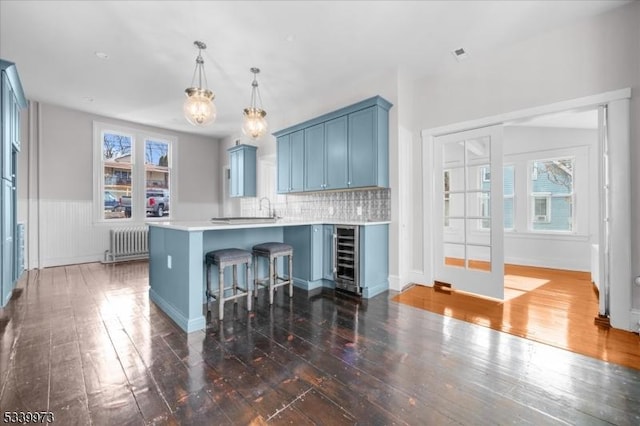 kitchen with blue cabinets, hardwood / wood-style floors, a peninsula, and radiator heating unit