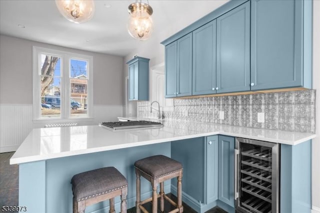 kitchen featuring wine cooler, blue cabinets, a peninsula, a breakfast bar, and wainscoting