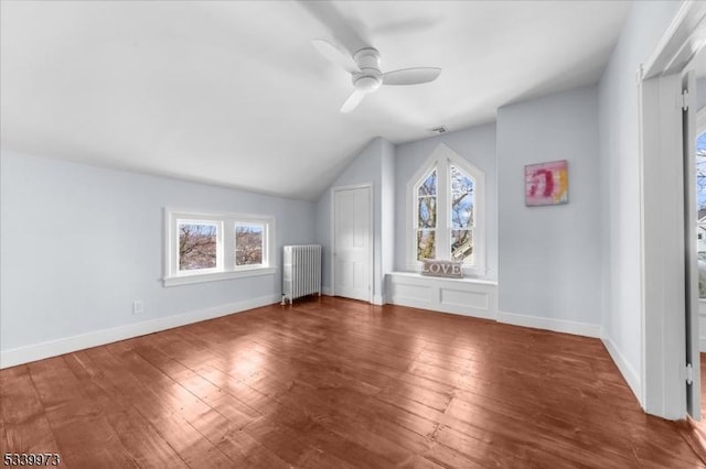 additional living space featuring radiator heating unit, wood-type flooring, a wealth of natural light, and baseboards