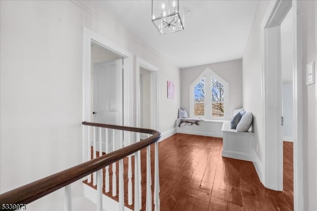 corridor featuring baseboards, dark wood finished floors, a notable chandelier, and an upstairs landing