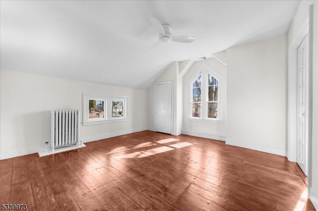 additional living space with ceiling fan, baseboards, vaulted ceiling, radiator, and wood-type flooring