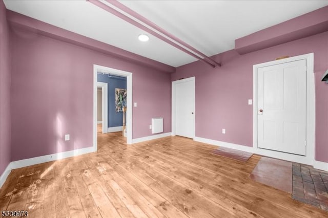 empty room with light wood-style floors, beamed ceiling, and baseboards