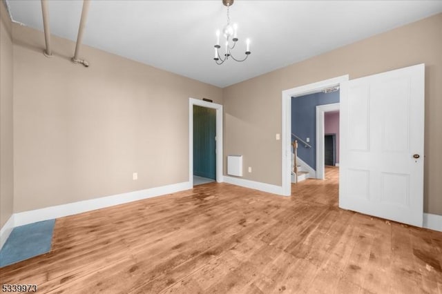 spare room with a chandelier, light wood finished floors, stairway, and baseboards