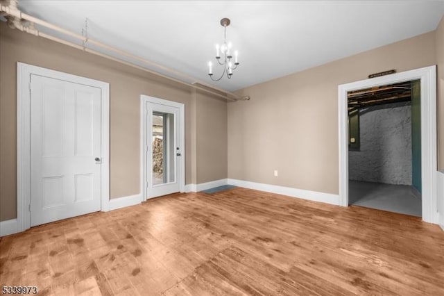 unfurnished bedroom with baseboards, light wood-type flooring, and an inviting chandelier