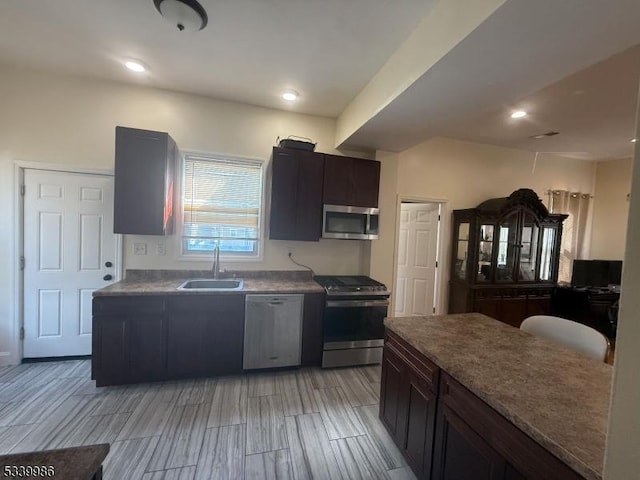 kitchen with stainless steel appliances, recessed lighting, wood tiled floor, a sink, and dark brown cabinetry