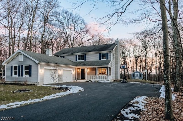 view of front of home featuring driveway, a garage, a chimney, a storage unit, and a porch