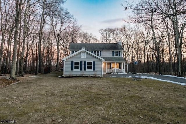 view of front of house with covered porch, a chimney, and a front yard