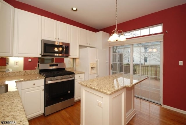 kitchen with a notable chandelier, stainless steel appliances, white cabinets, a kitchen island, and wood finished floors