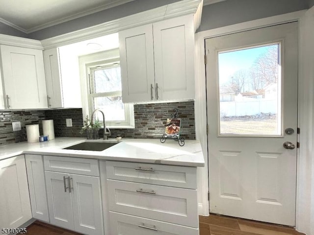 kitchen featuring crown molding, white cabinetry, backsplash, and a sink