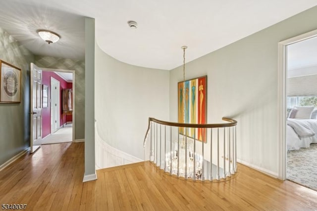 corridor with baseboards, an upstairs landing, and wood finished floors