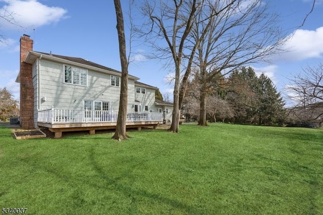 back of house featuring a wooden deck, a lawn, and a chimney