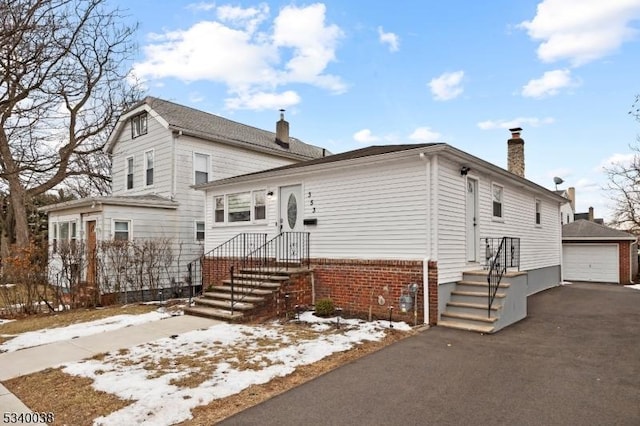 view of front of house with an outbuilding, aphalt driveway, brick siding, a detached garage, and a chimney