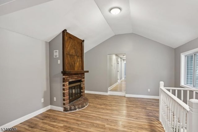 living area featuring vaulted ceiling, a brick fireplace, wood finished floors, and baseboards