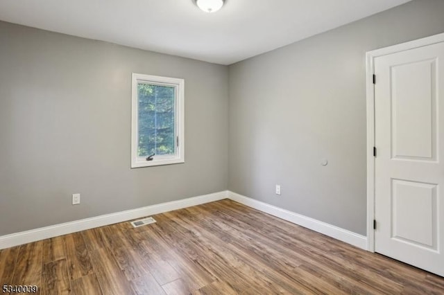 unfurnished room featuring baseboards, visible vents, and wood finished floors