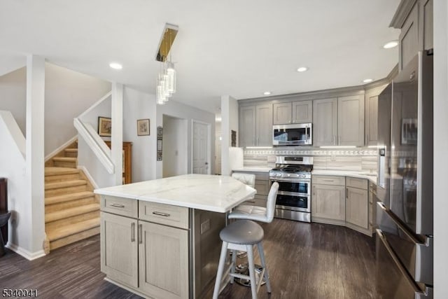 kitchen featuring gray cabinetry, dark wood-style flooring, appliances with stainless steel finishes, backsplash, and a center island