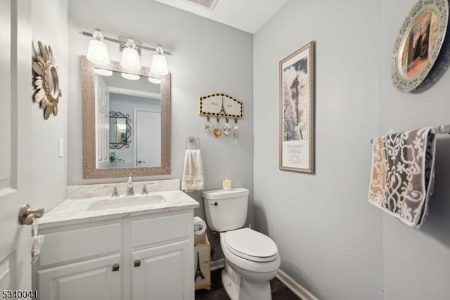 half bath with toilet, baseboards, and vanity