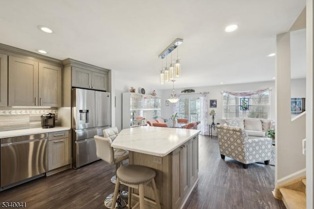 kitchen with stainless steel appliances, a kitchen island, open floor plan, light countertops, and dark wood-style floors