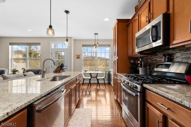 kitchen with light stone counters, brown cabinets, stainless steel appliances, tasteful backsplash, and a sink