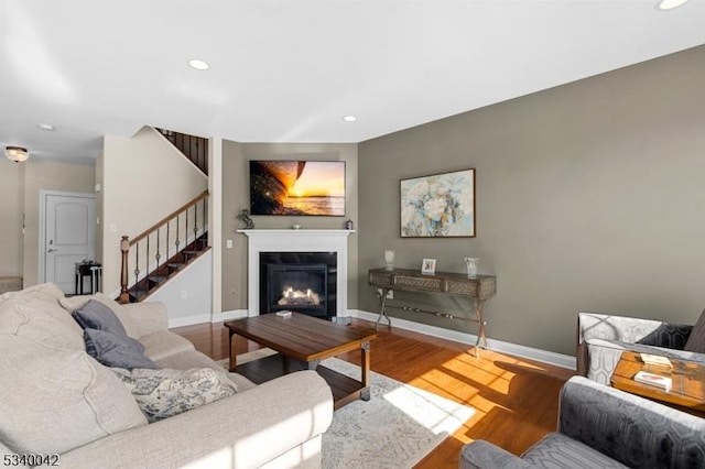 living area featuring recessed lighting, a glass covered fireplace, wood finished floors, baseboards, and stairs