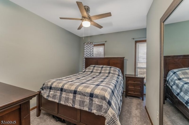 bedroom featuring light carpet, multiple windows, baseboards, and a ceiling fan