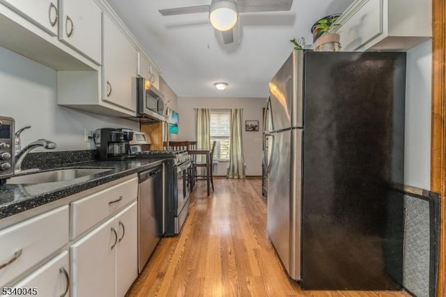 kitchen with appliances with stainless steel finishes, light wood-type flooring, white cabinets, and a sink