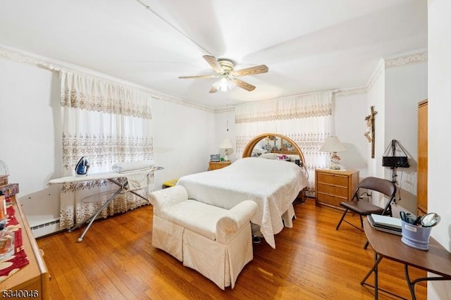 bedroom featuring ceiling fan, a baseboard heating unit, wood finished floors, and crown molding