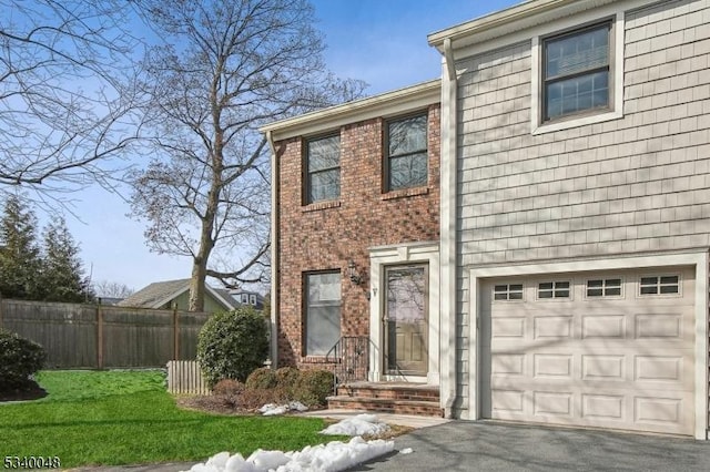 view of front of home featuring aphalt driveway, brick siding, a front yard, fence, and a garage