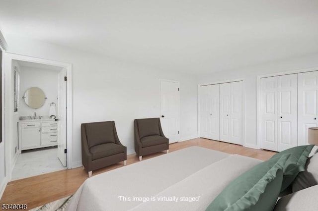 bedroom featuring ensuite bath, light wood-type flooring, and two closets