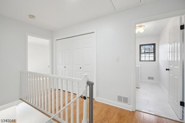 hall with light wood finished floors, baseboards, visible vents, and an upstairs landing