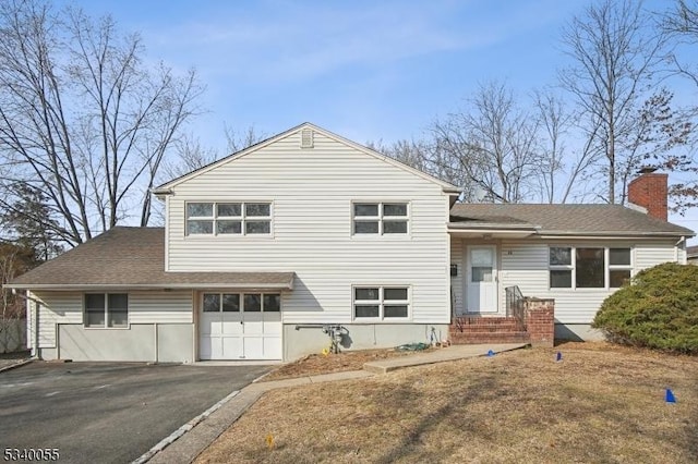 tri-level home with an attached garage, a shingled roof, a chimney, and aphalt driveway