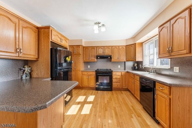 kitchen featuring light wood-style floors, dark countertops, under cabinet range hood, black appliances, and a sink