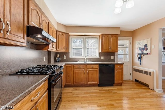 kitchen with light wood-style flooring, under cabinet range hood, a sink, black appliances, and radiator heating unit