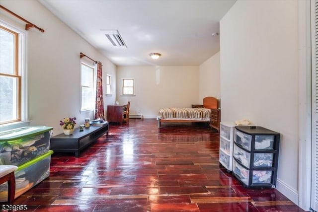 bedroom with a baseboard heating unit, dark wood-style flooring, visible vents, and baseboards