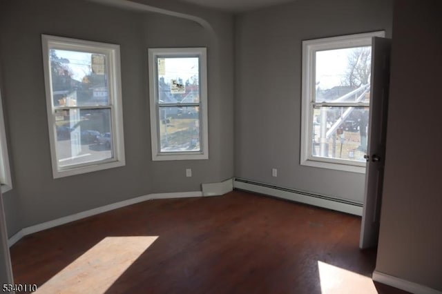 empty room with dark wood-style flooring, baseboard heating, and baseboards