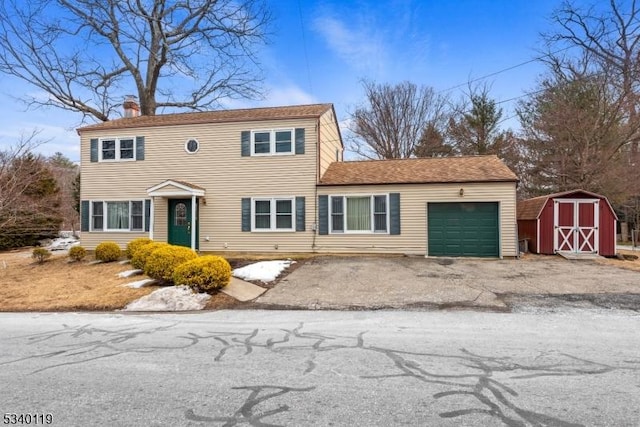 colonial inspired home featuring a garage, a chimney, aphalt driveway, a storage unit, and an outdoor structure