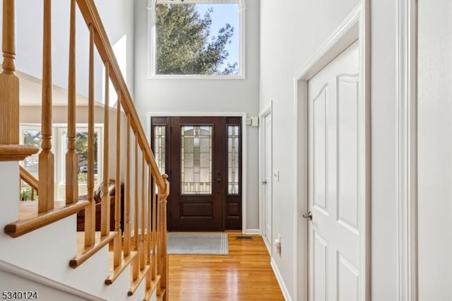 foyer entrance with a towering ceiling, light wood finished floors, stairs, and baseboards