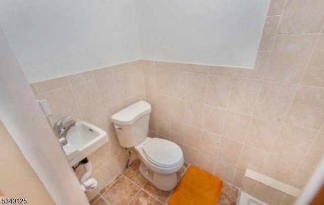 half bathroom featuring tile patterned flooring, a sink, toilet, and tile walls