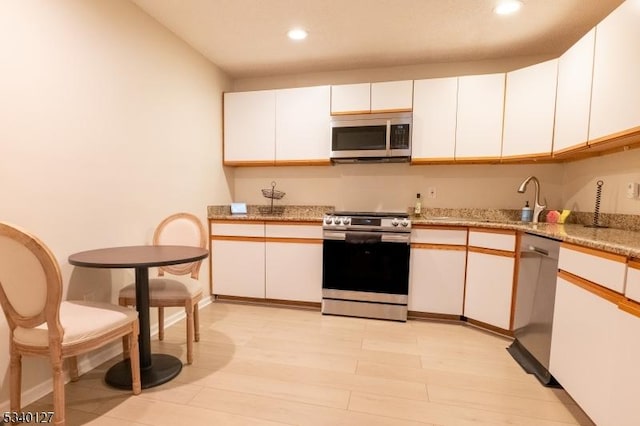 kitchen with light wood-style flooring, appliances with stainless steel finishes, white cabinetry, a sink, and recessed lighting