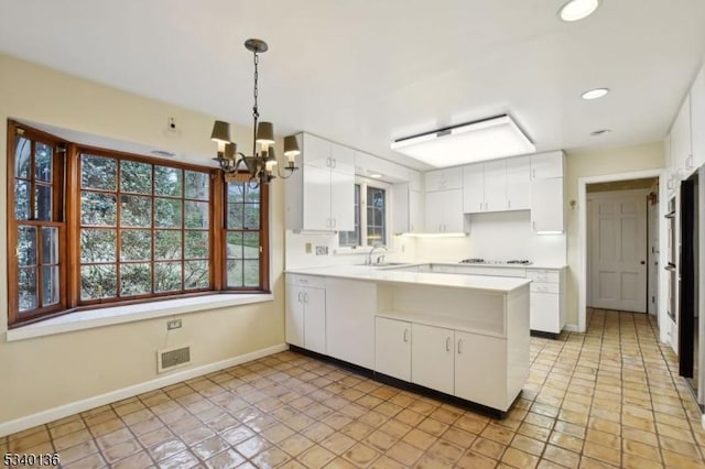 kitchen with light countertops, white cabinets, a sink, and a peninsula