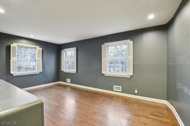 spare room featuring wood finished floors, visible vents, and baseboards