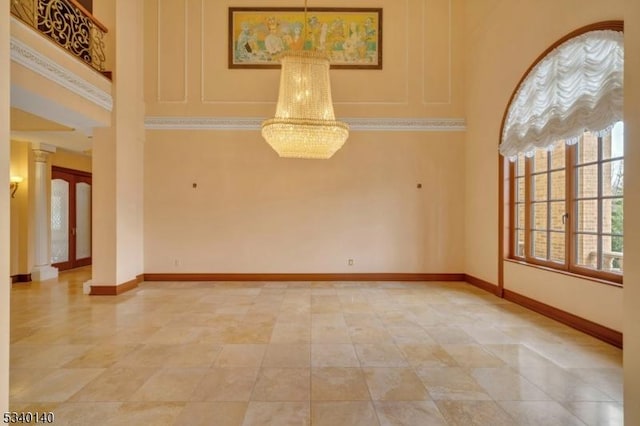 empty room with a high ceiling, decorative columns, a notable chandelier, and baseboards