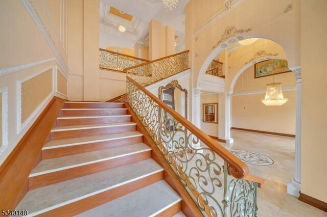 stairway with decorative columns, arched walkways, tile patterned floors, a high ceiling, and a decorative wall