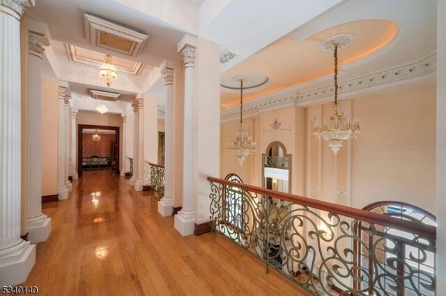 corridor with wood finished floors, a tray ceiling, crown molding, an upstairs landing, and ornate columns