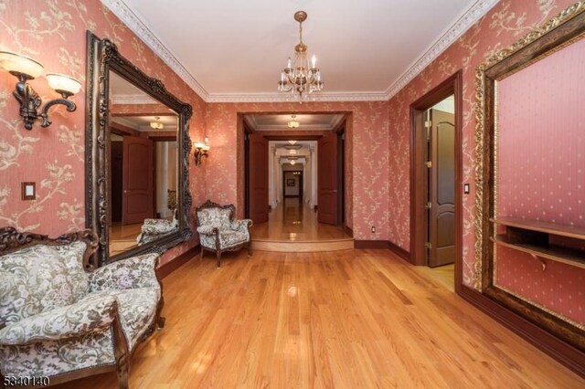 corridor with a notable chandelier, ornamental molding, wood finished floors, baseboards, and wallpapered walls