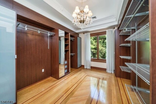 walk in closet with a tray ceiling, wood finished floors, visible vents, and a notable chandelier