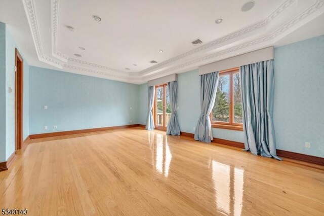 empty room with a tray ceiling, crown molding, visible vents, light wood-style flooring, and baseboards