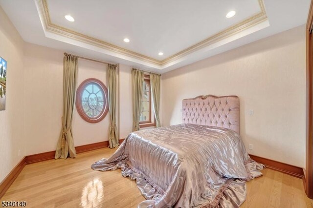 bedroom with a tray ceiling, recessed lighting, ornamental molding, light wood-type flooring, and baseboards