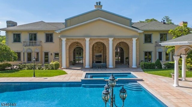 back of property with a patio, a chimney, a pool with connected hot tub, and stucco siding