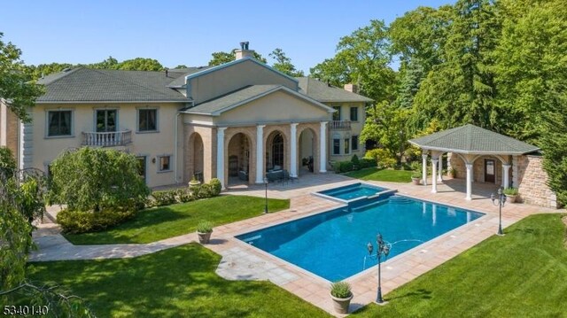 rear view of house featuring an outdoor pool, a balcony, an in ground hot tub, a yard, and a patio area